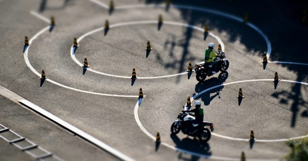 教習所のコースで、パイロンの間を2台のバイクが走っている二輪教習の様子