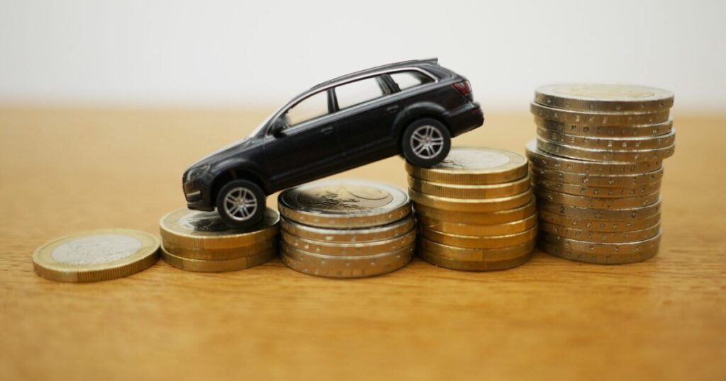 少しずつ高く積まれた硬貨の上をのぼる、車の模型